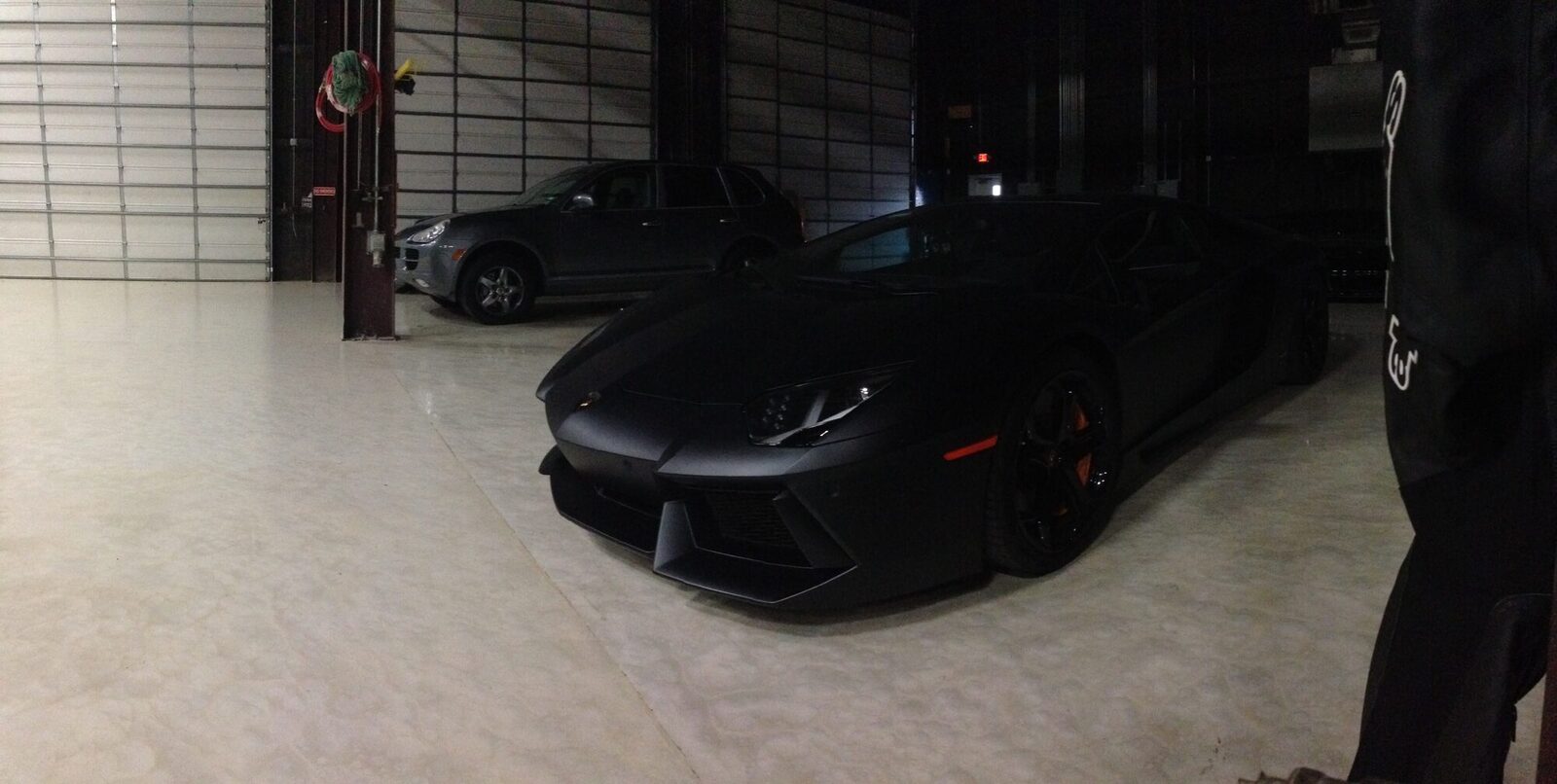 A matte black Lamborghini Aventador parked inside a dim shop